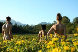 3 people stand naked in a field of flowers